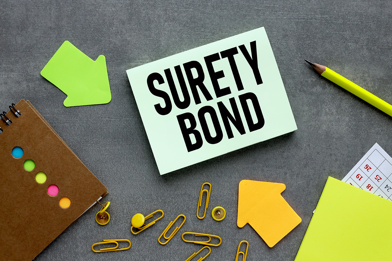 Text,On,Green,Sticker.,On,A,Gray,Background,Near,Bright text on green sticker. on a gray background near bright stickers and paper clips SURETY BOND. Business concept